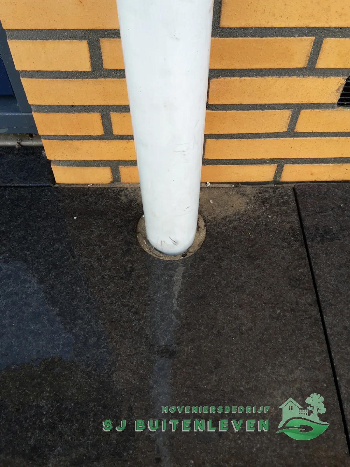 Detailfoto van nauwkeurig rondom een regenpijp gezaagde terrastegels tegen de bakstenen gevel van een woning in Heerhugowaard.