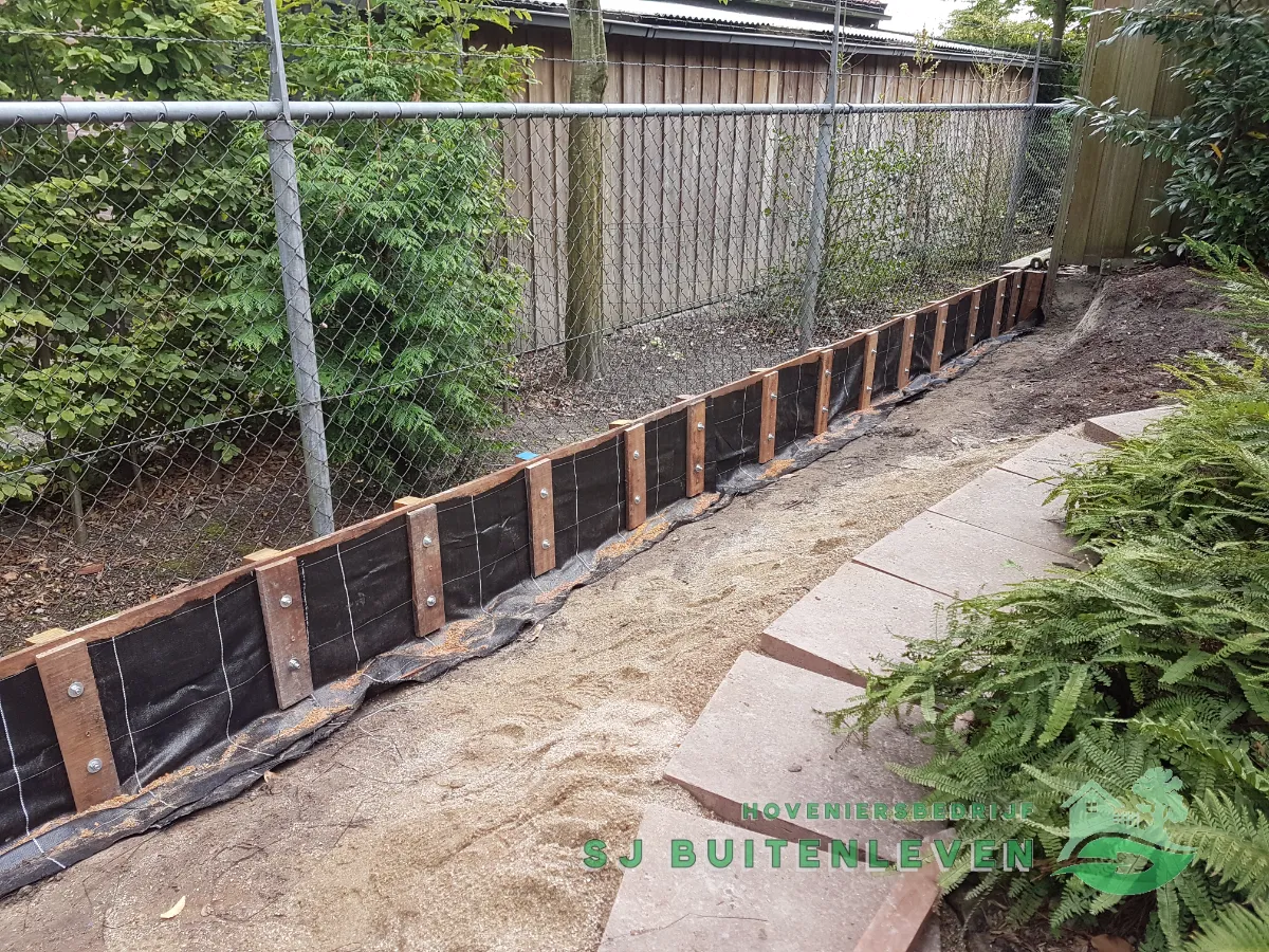 Afgewerkte grondkering langs de erfafscheiding met onregelmatige stapstenen als pad tussen de varens in Nieuwe Niedorp.