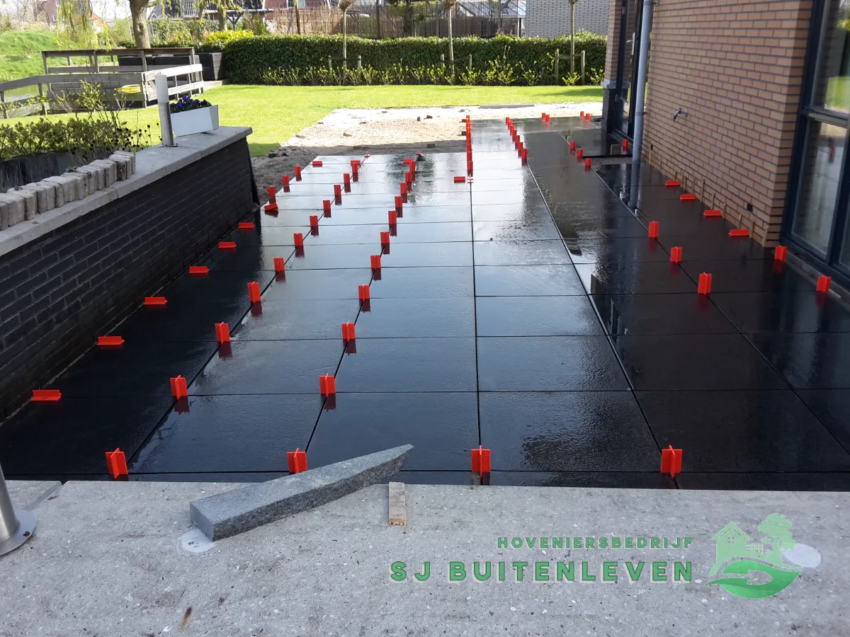 Terras in aanbouw in Heerhugowaard gezien vanaf de opstap, met een natuurstenen muurrand en een losse boordsteen die nog geplaatst moet worden.