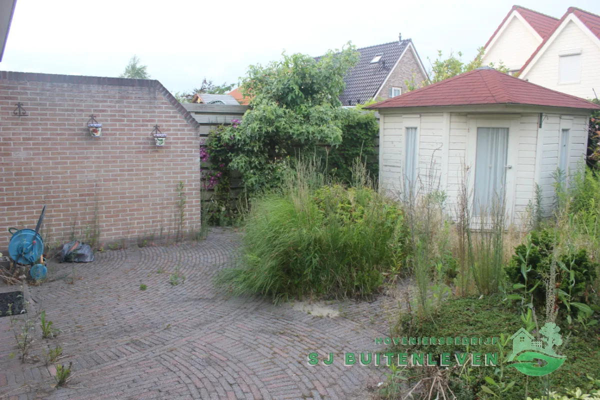 Verwaarloosde bakstenen patio met onkruid tussen de voegen en een wit tuinhuisje, de bestaande situatie bij deze tuin in Heerhugowaard.