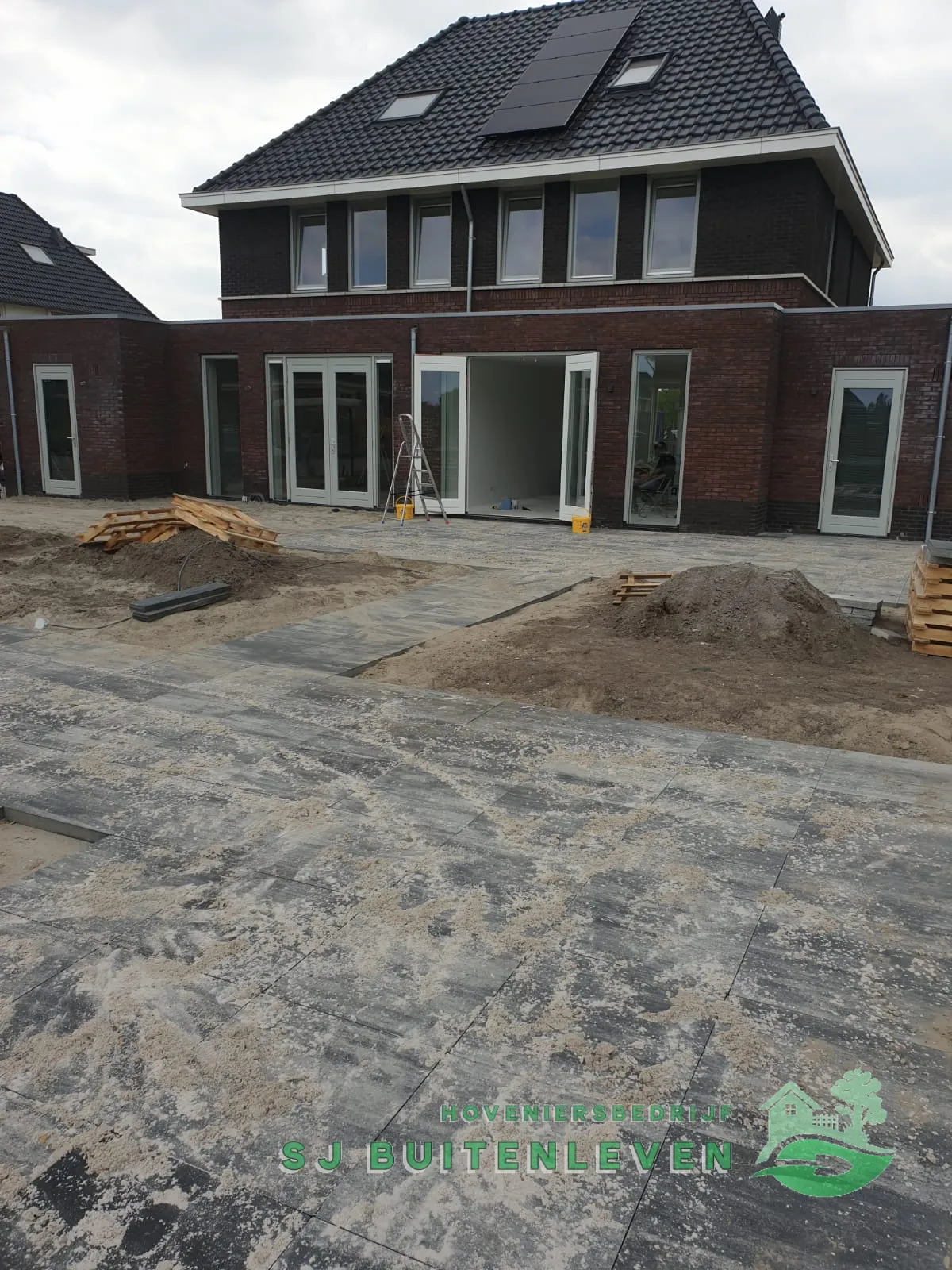 Groot terras met antracietkleurige tegels in aanleg tegen de achtergevel van de vrijstaande villa in Spanbroek.