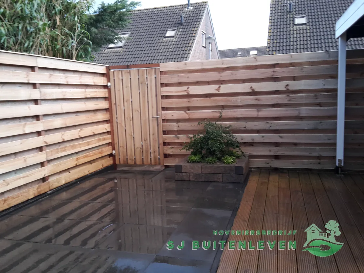 Gesloten houten poortdeur in de horizontale schutting, met overgang van terrastegels naar houten vlonder in Hoorn.