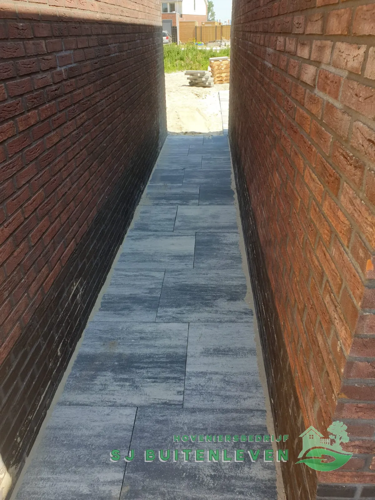 Smal bestraat zijpad tussen de woning en het buurpand bij deze tuinaanleg in Spanbroek.