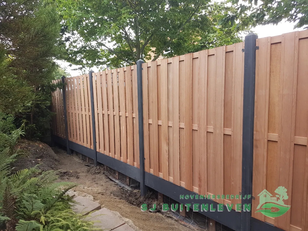 Volledige lengte van de nieuwe schutting met houten planken op zwarte onderplaat, langs het tuinpad in Nieuwe Niedorp.