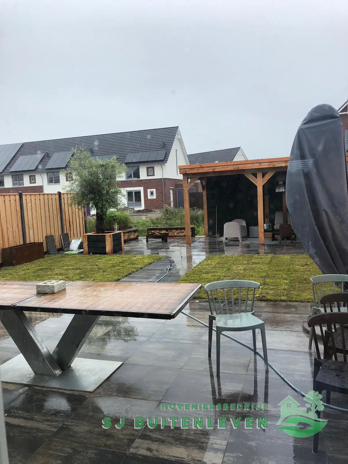 Afgeronde tuin in Spanbroek met houten pergola, olijfboom in plantenbak en vers aangelegd gazon.