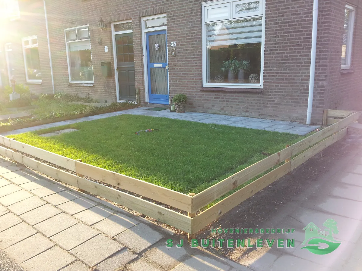 Nieuw aangelegd gazon met houten hekwerk en grijs bestraat pad naar de voordeur, project Voortuin Renovatie in Slootdorp door hovenier SJ Buitenleven (eindresultaat)