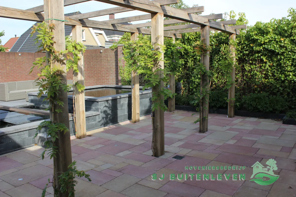 Nieuwe houten pergola met beplanting boven de verhoogde vijver en het natuurstenen terras in Heerhugowaard door hovenier SJ Buitenleven (eindresultaat).