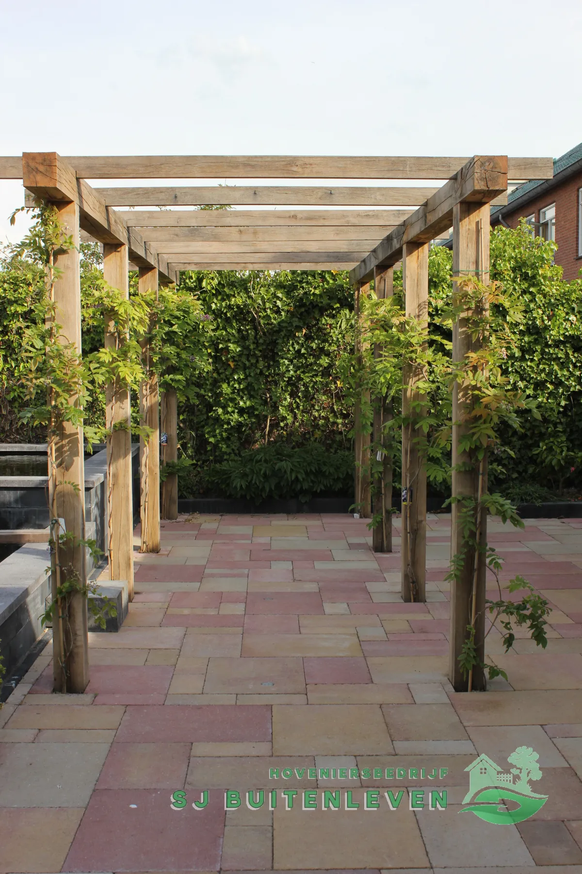Robuuste eikenhouten pergola met opkomende klimplanten boven het nieuwe terras van de tuinrenovatie in Heerhugowaard.