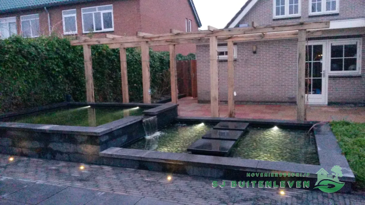 Verlichte vijver en pergola bij avond, gezien vanaf het terras bij de tuindeur van de woning in Heerhugowaard.